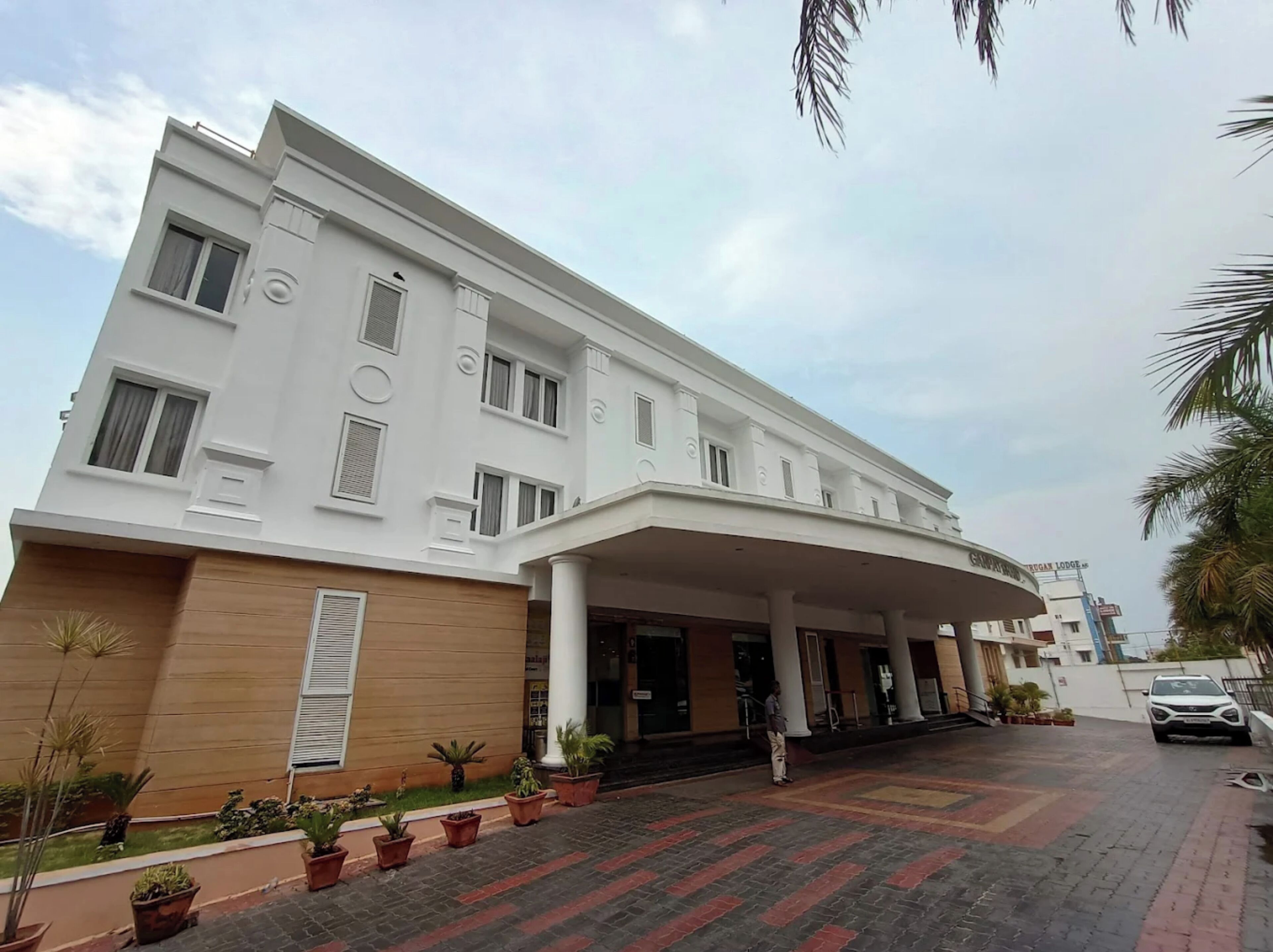 A modern hotel with a white facade, a covered entrance, and a paved driveway with potted plants.