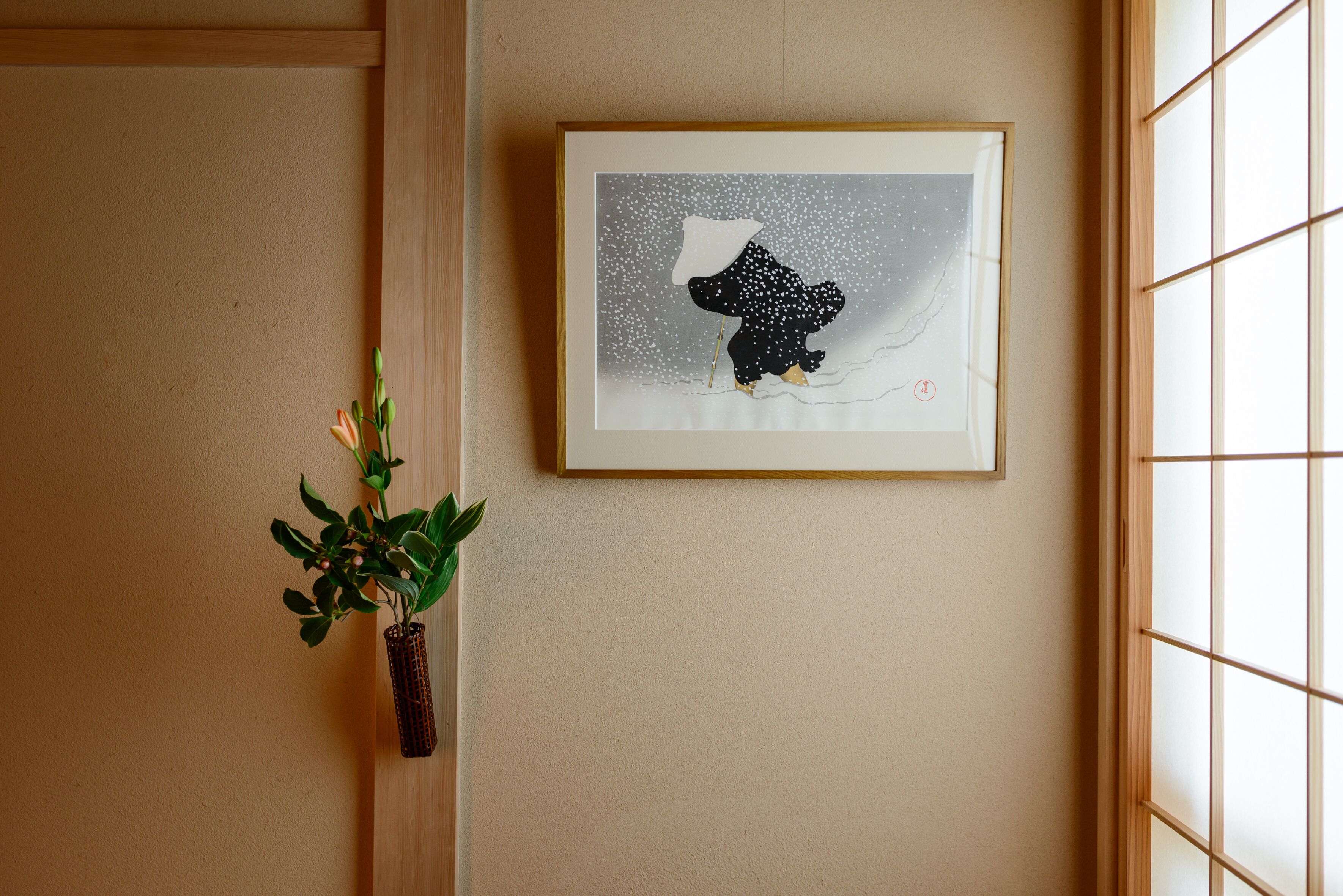 A framed artwork of a bear on a snowy background, a potted plant, and a window with a grid pattern.