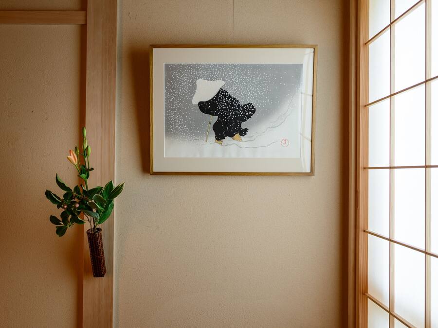 A framed artwork of a bear on a snowy background, a potted plant, and a window with a grid pattern.