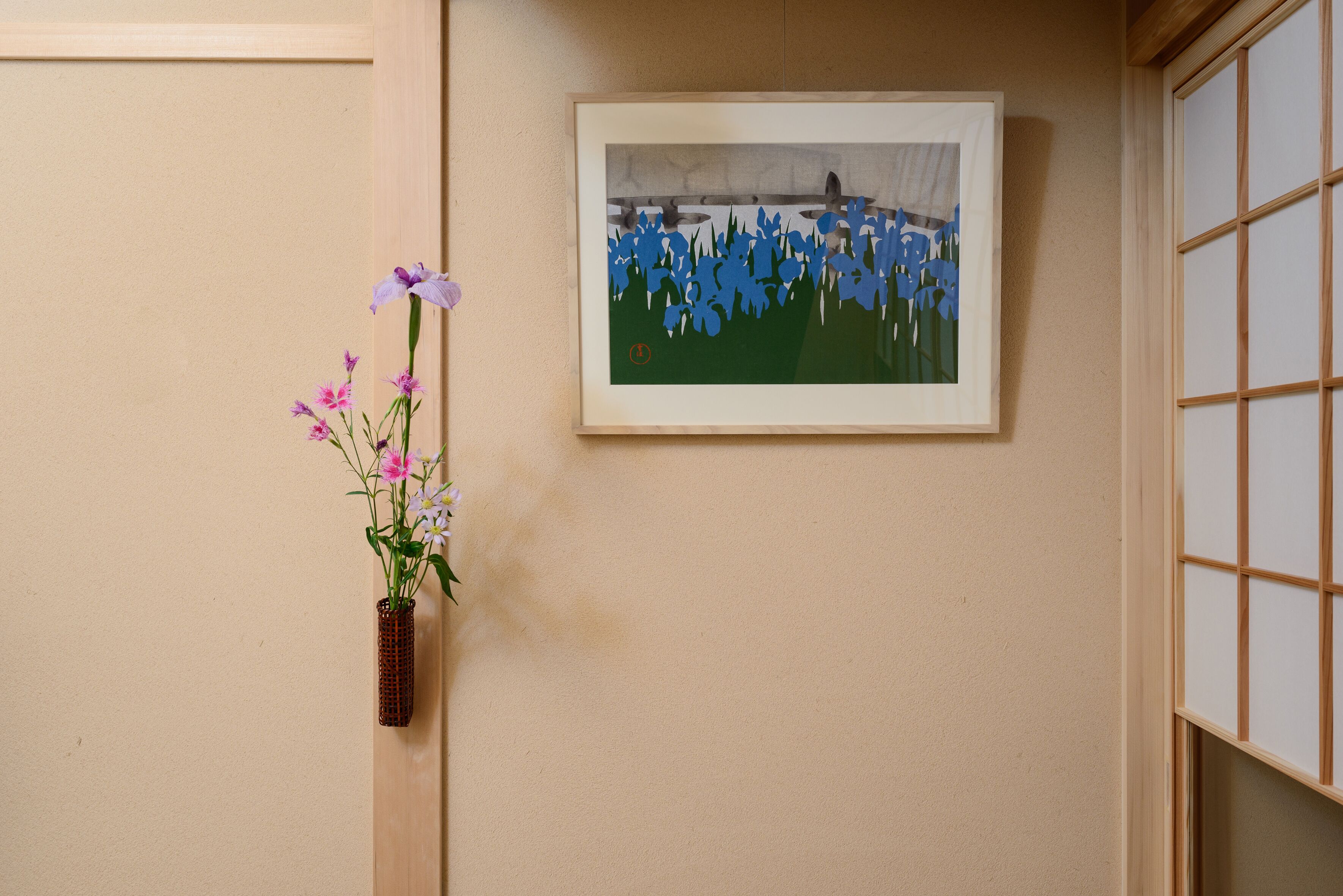 A framed artwork on a beige wall, a vase with flowers on a wooden surface, and a traditional sliding door.