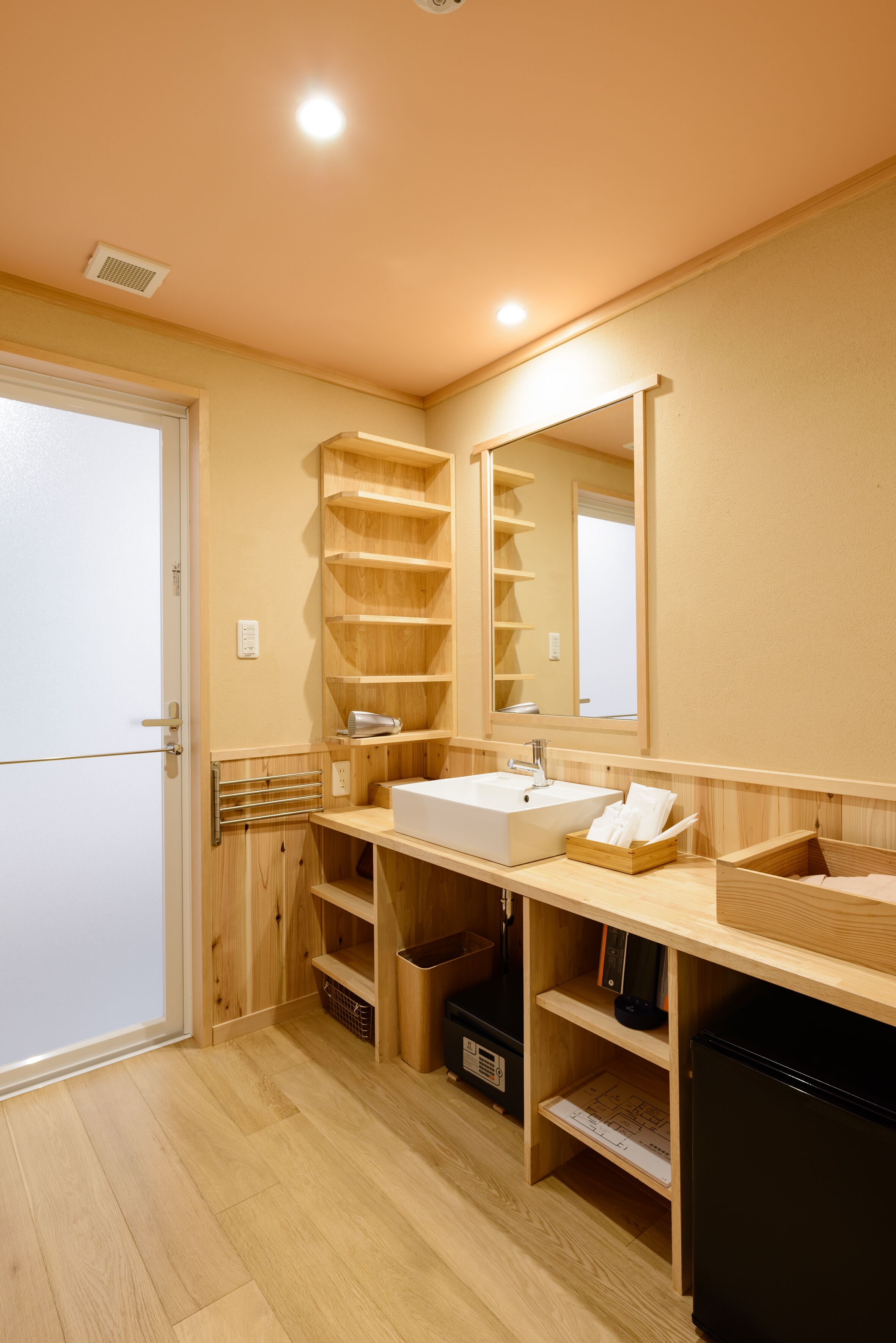 A modern bathroom with a wooden vanity, a large mirror, and built-in shelves.