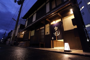 Un edificio japonés tradicional con fachada de madera, una entrada visible y un cartel con caracteres japoneses.