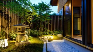 A modern building with a large glass facade, a stone lantern, and a well-maintained garden with rocks and plants. - Luck You Kyoto (Kyoto)