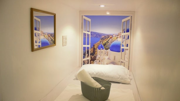 A hotel room with a bed, a basket, and a large window with a view of a coastal town. - Shejoje Poshtel Hostel (Cebu City)
