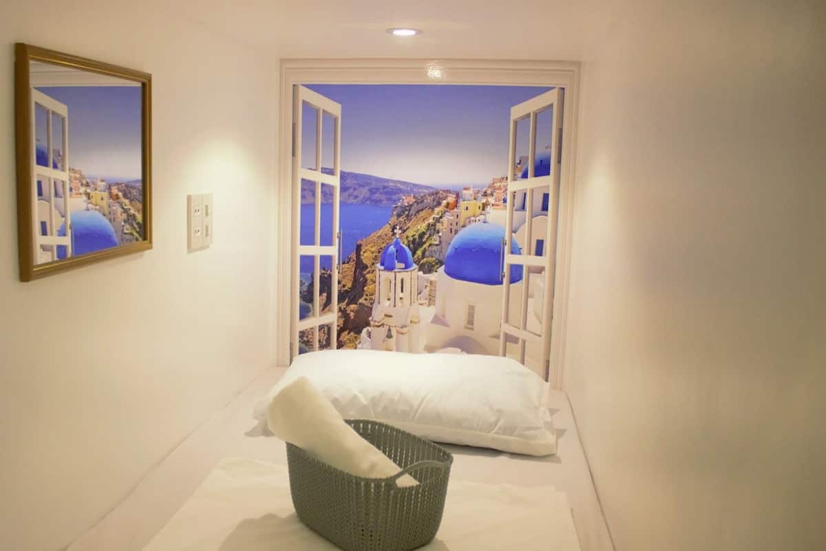 A hotel room with a bed, a basket, and a large window with a view of a coastal town.
