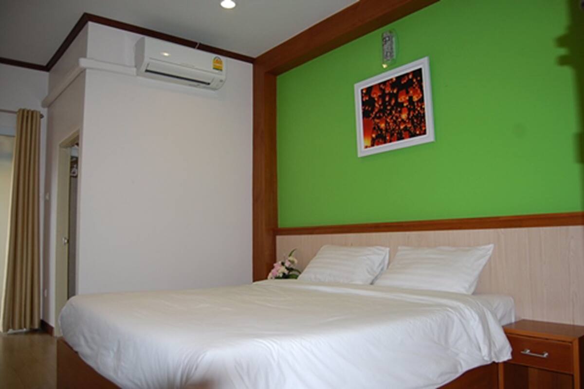 Una habitación de hotel con una cama, una mesita de noche, aire acondicionado instalado en la pared y un cuadro en la pared verde.