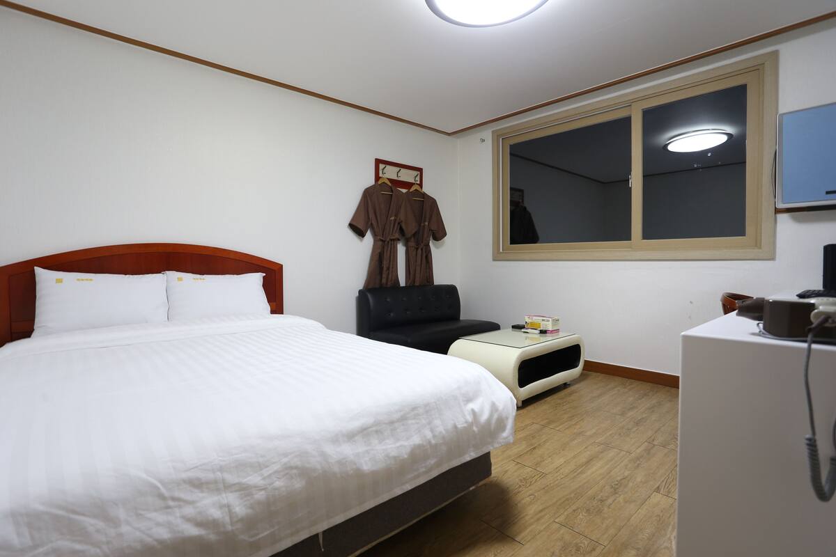 A hotel room with a large bed, a small desk, a chair, a wardrobe, and a mirror.