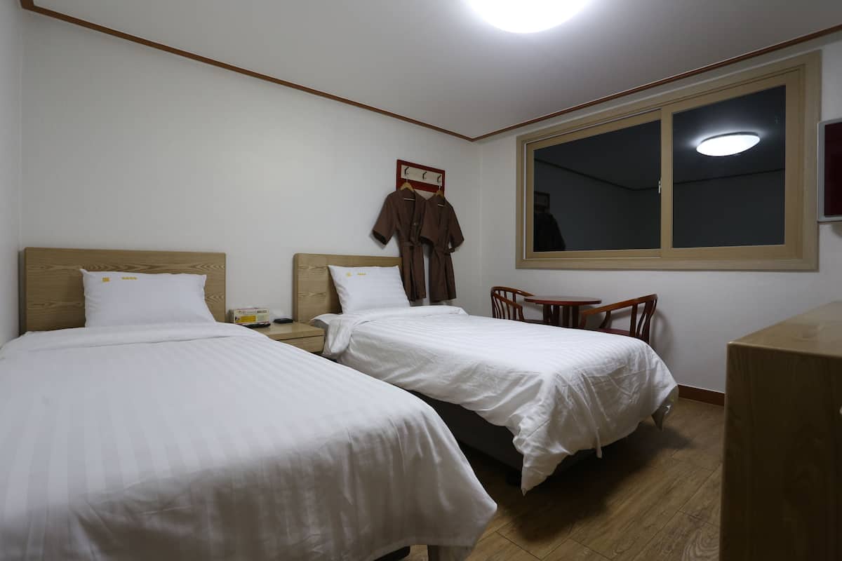 A hotel room with two beds, a wooden headboard, a nightstand, a wooden table, and a window with a view.