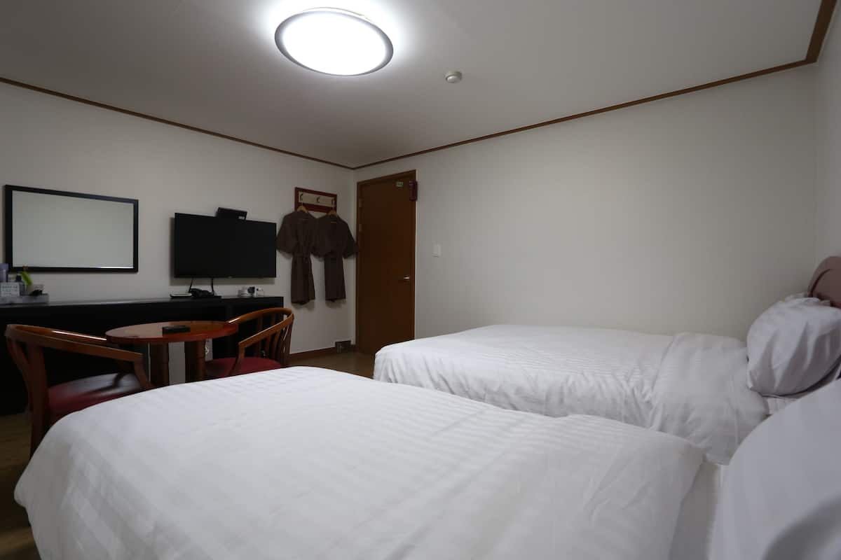 A hotel room with two beds, a desk with a chair, a television, and a coat rack.