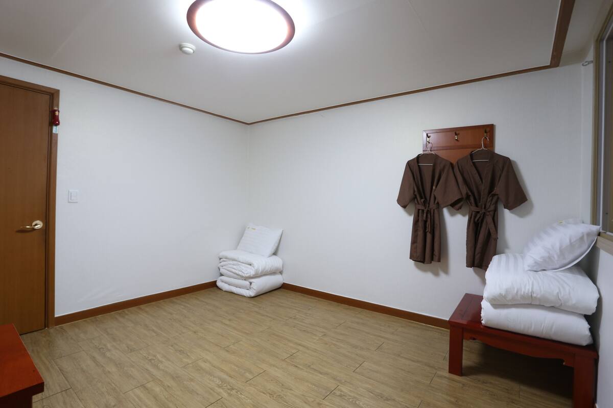 A room with a wooden floor, a door, a bench, and a wall-mounted robe rack with towels.