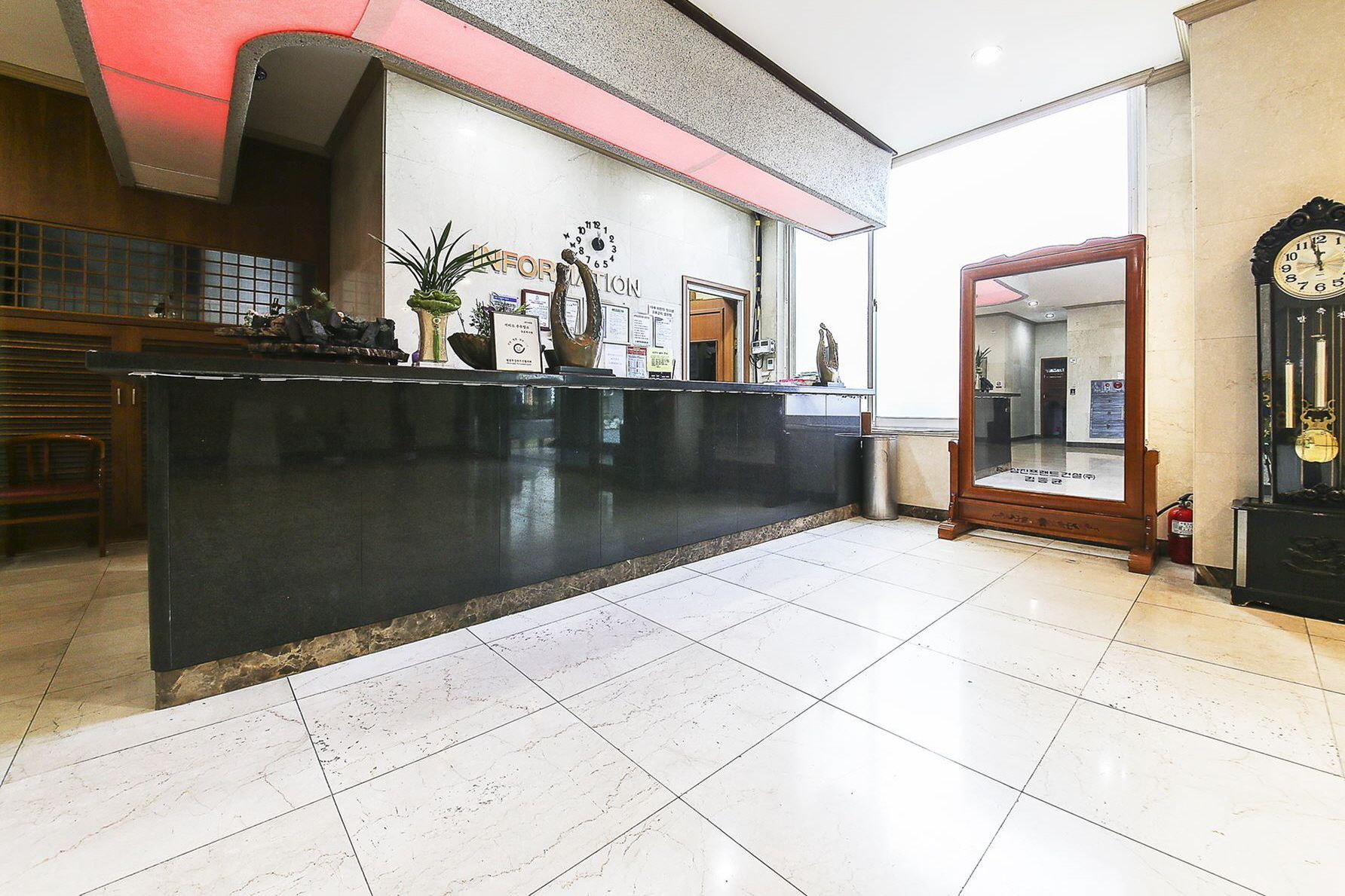 Zona de recepción de un hotel con un mostrador negro, un espejo grande y un reloj en la pared.