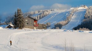 Une piste de ski enneigée, avec un bâtiment doté d’un toit rouge et un télésiège en arrière-plan.