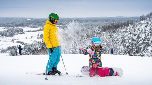 A snowy ski slope with two skiers, one adult and one child, and a snowboarder.