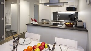 Une cuisine moderne avec un plan de travail noir, des meubles blancs et un coin repas avec une table dressée pour deux personnes.