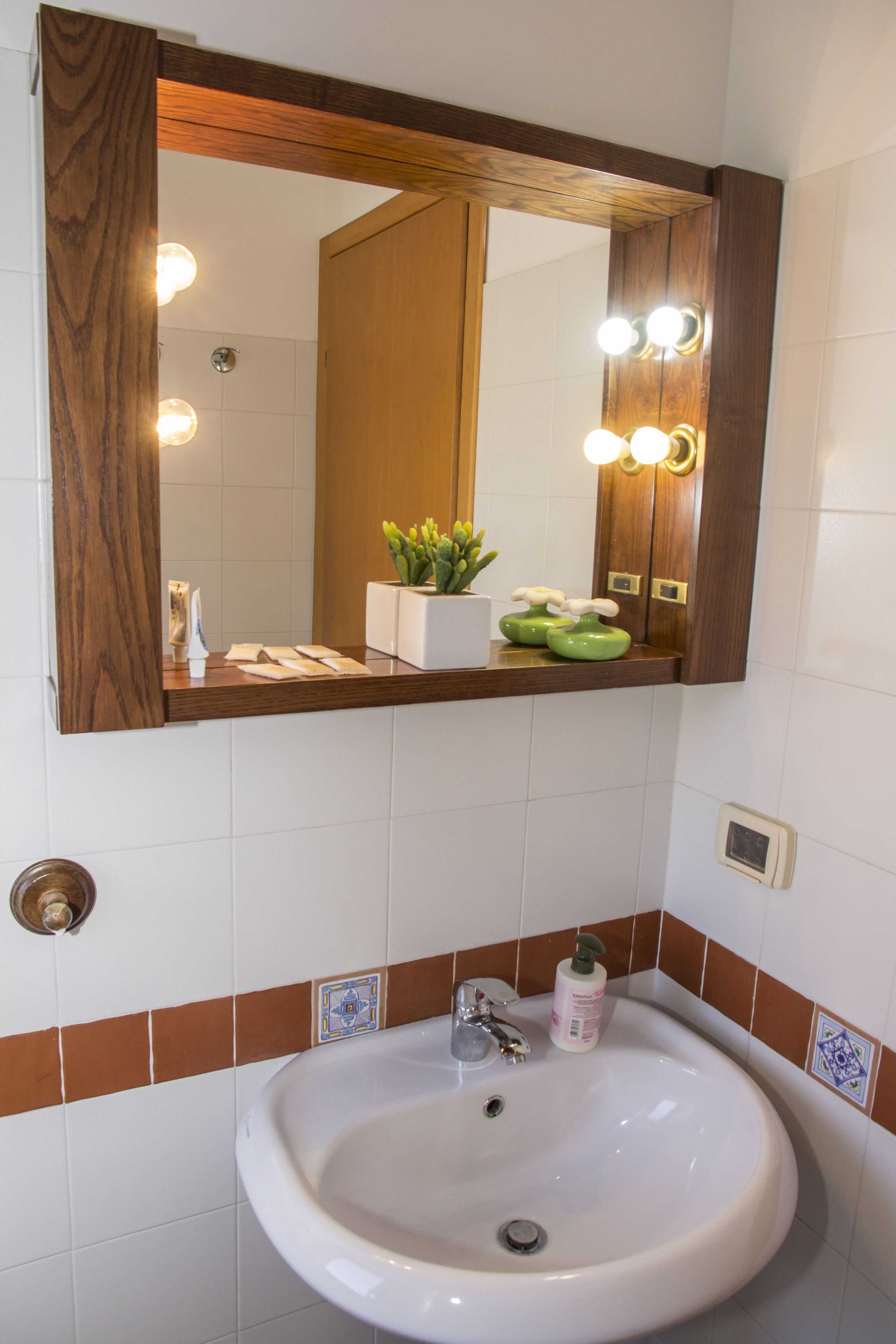 A bathroom with a white sink, a wooden vanity, a mirror with lights, and a small plant.