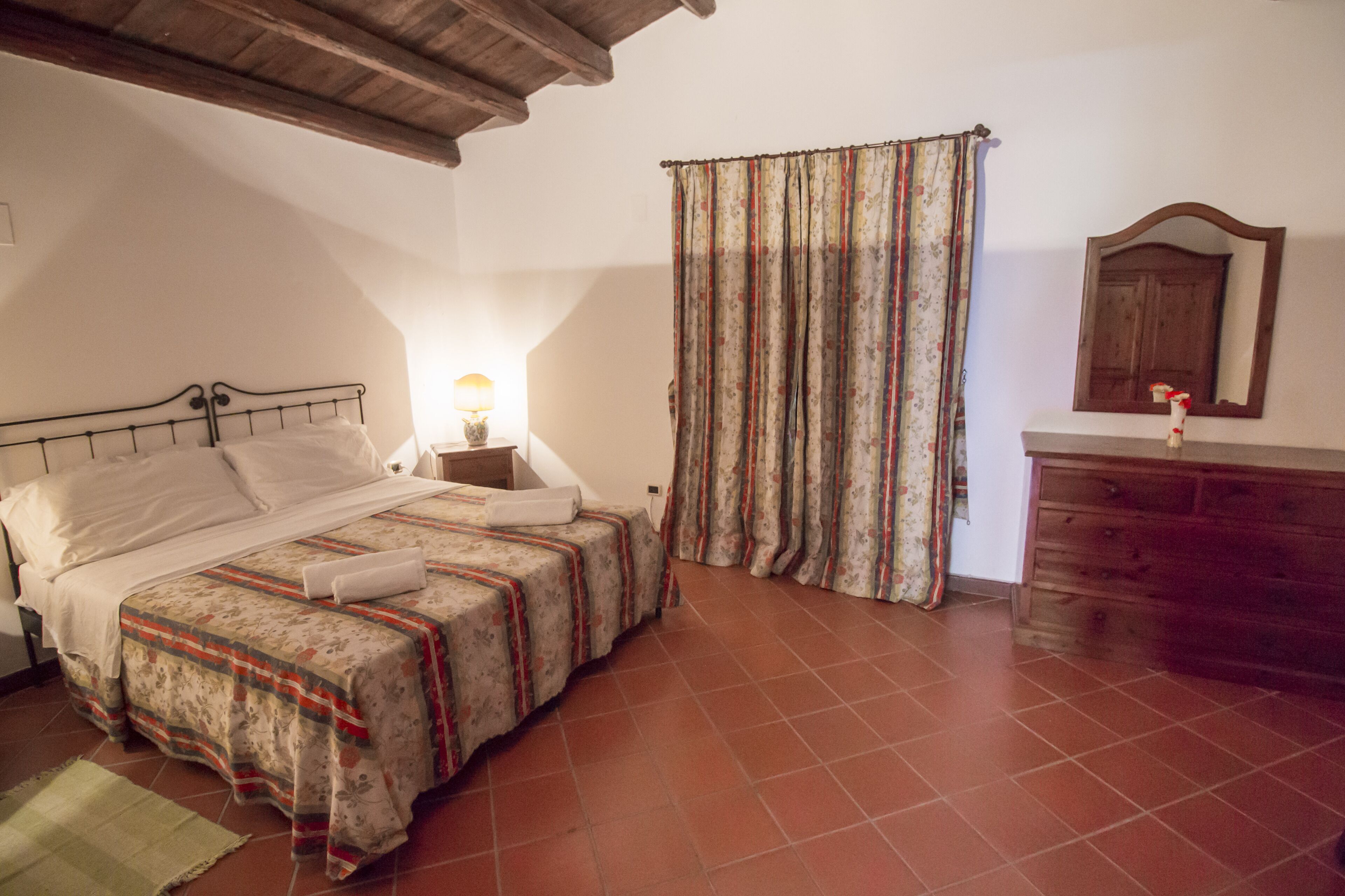 Un dormitorio con cama, mesita de noche, cómoda, espejo y ventana con cortinas.