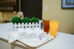 A tray with rolled towels and two glasses of beverages on a hotel counter.