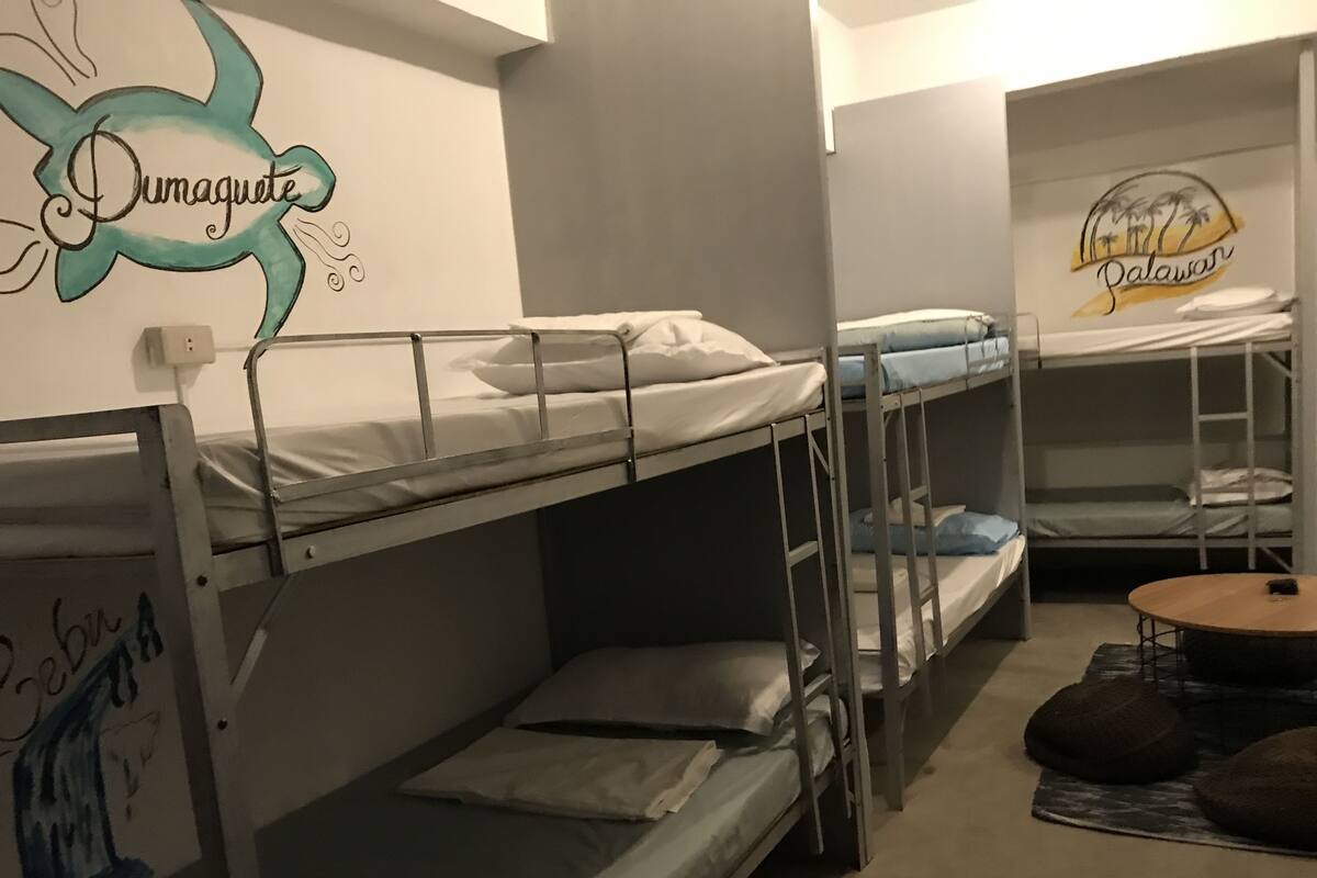 A dormitory room with bunk beds, a wall mural, and a small round table.