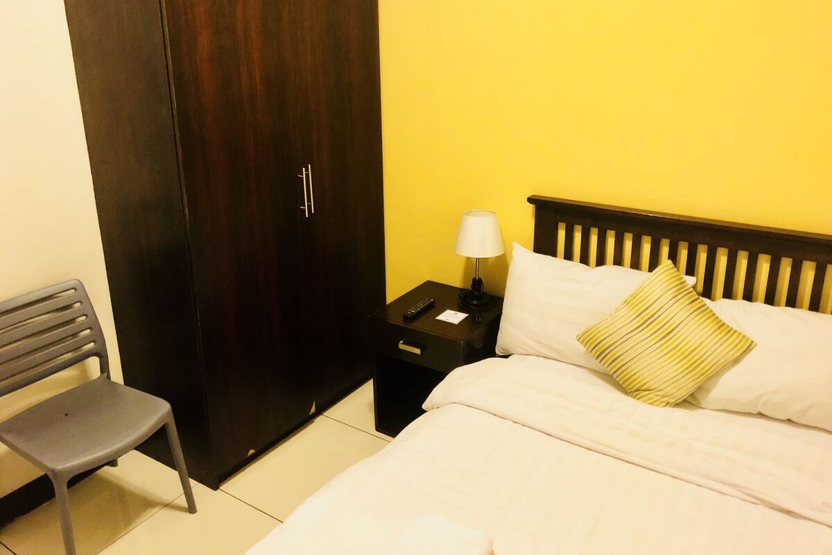 A hotel room with a bed, a nightstand, a lamp, a chair, and a wardrobe.