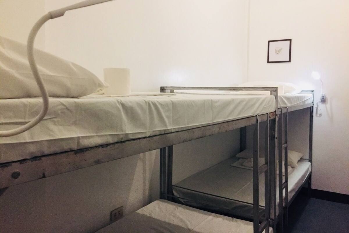A bunk bed room with a single bed and a bunk bed. There is a wall-mounted light fixture and a framed picture on the wall.