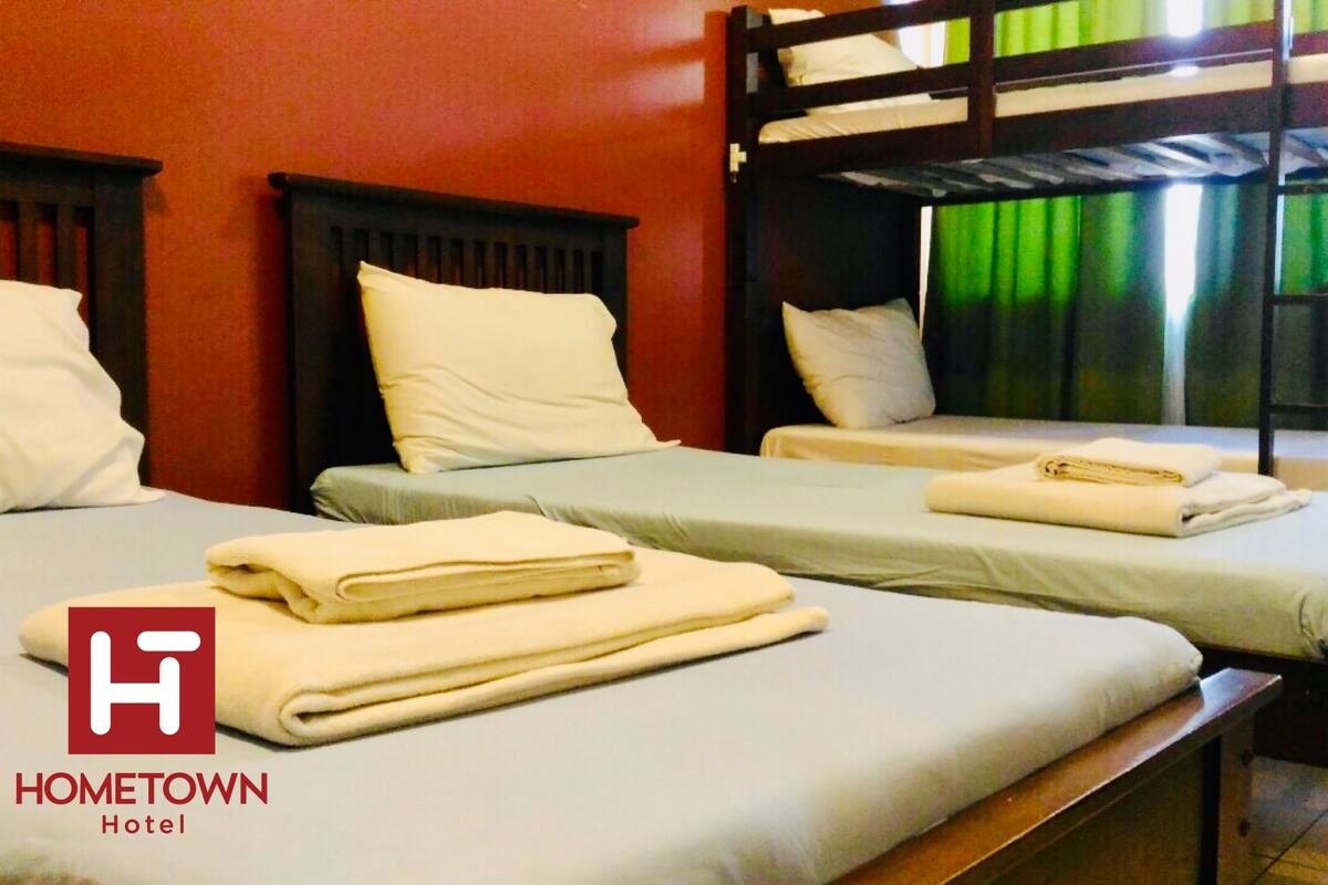 A room with bunk beds, each with a pillow and a folded towel. The room has a red wall and a window with green curtains.