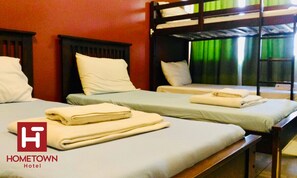 A room with bunk beds, each with a pillow and a folded towel. The room has a red wall and a window with green curtains.
