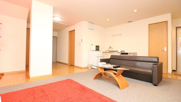 A modern living room with a grey sofa, a red rug, and a glass coffee table. - BK Hotel & Weekly (Wakayama)
