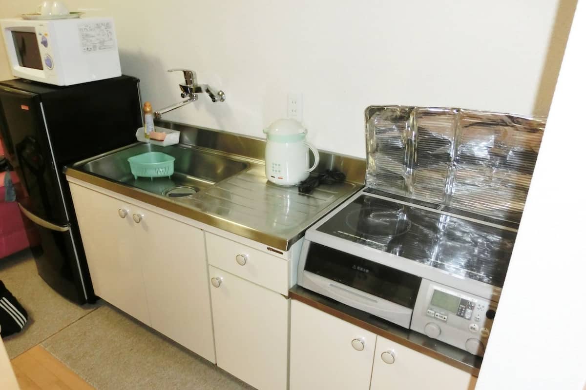 Una cocina compacta con un lavamanos, un microondas, una tetera y una estufa.