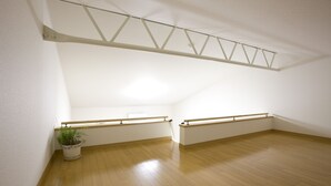 A room with wooden flooring, white walls, and a sloped ceiling. There is a potted plant in the corner and a window with a metal frame. - BK Hotel & Weekly (Wakayama)