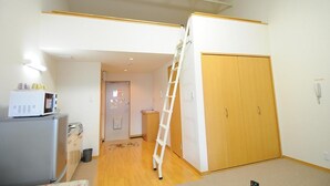 A room with a wooden wardrobe, a white refrigerator, a microwave, and a white ladder leaning against the wall. - BK Hotel & Weekly (Wakayama)