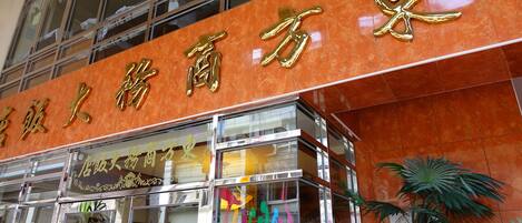 A building with a large sign in Chinese characters, a glass storefront, and a palm tree in front.