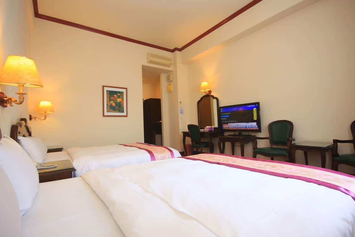 Habitación de hotel con dos camas, un escritorio con computadora y televisor.