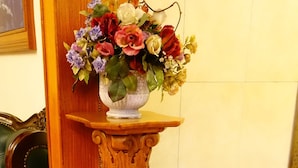 Um pedestal de madeira com arranjo floral, uma escultura de elefante entalhada e uma cadeira estofada verde.