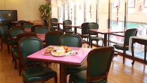 Um restaurante com mesas e cadeiras de madeira, uma televisão na parede e uma janela decorada.