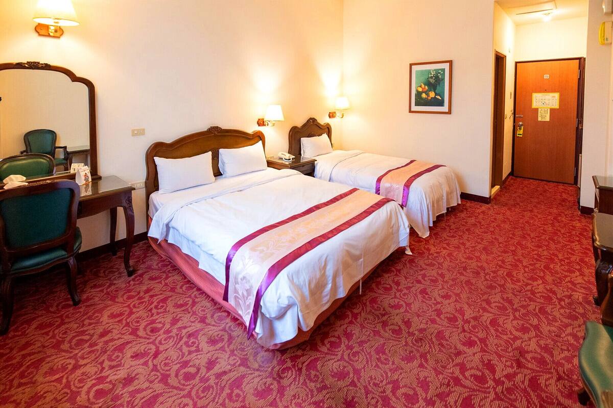 Una habitación de hotel con dos camas, un espejo, un escritorio y una puerta.