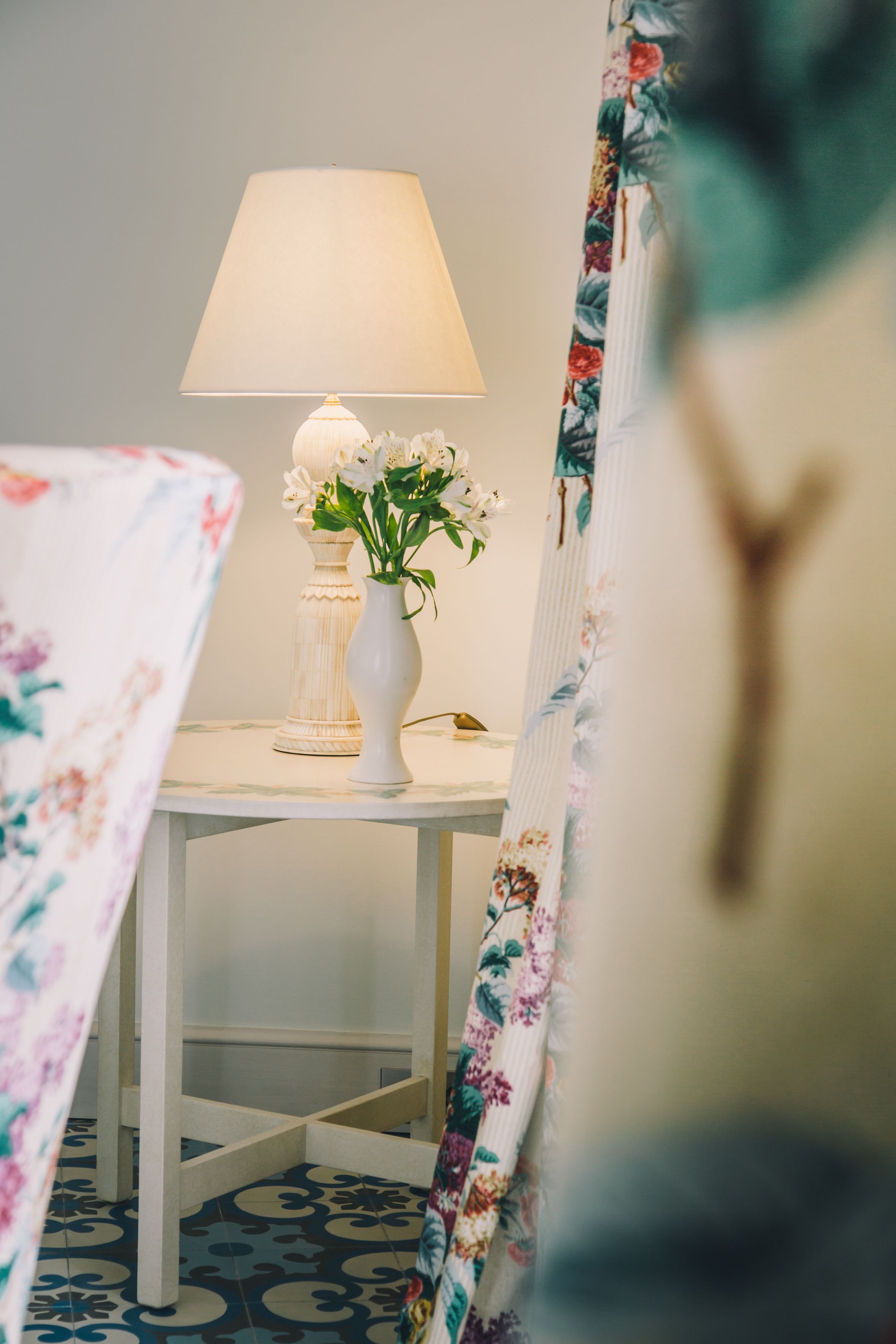Una habitación con una mesa que tiene una lámpara y un florero con flores.
