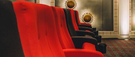 Hileras de asientos rojos y negros estilo teatro, con alfombra estampada y decoración de rayos de sol en la pared.
