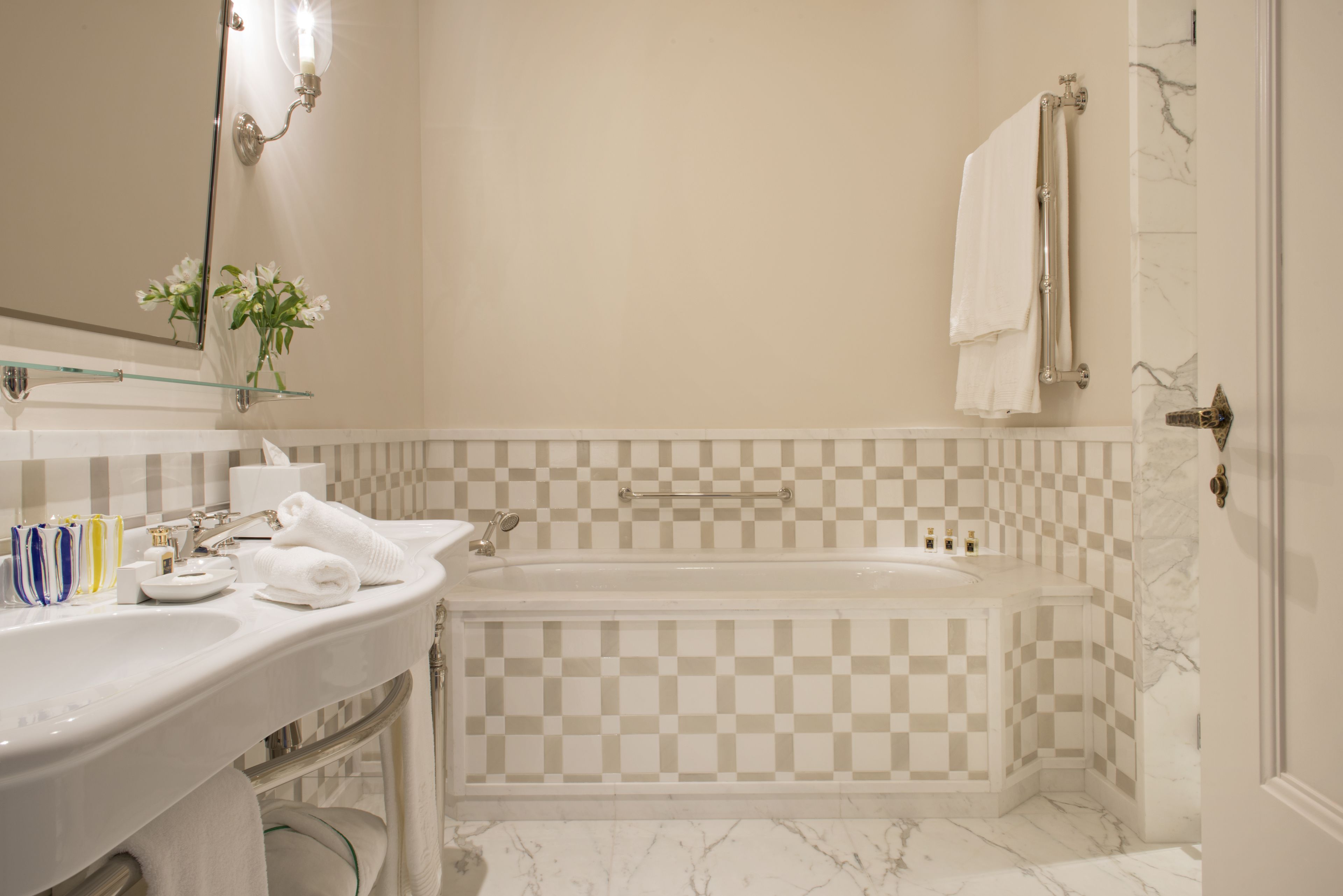 Um banheiro com parede de azulejos quadriculada, banheira, pia com prateleira de vidro e espelho com luminária.