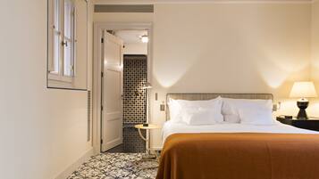Habitación de hotel con cama, mesita de noche, lámpara, suelo estampado y puerta que da a un baño.