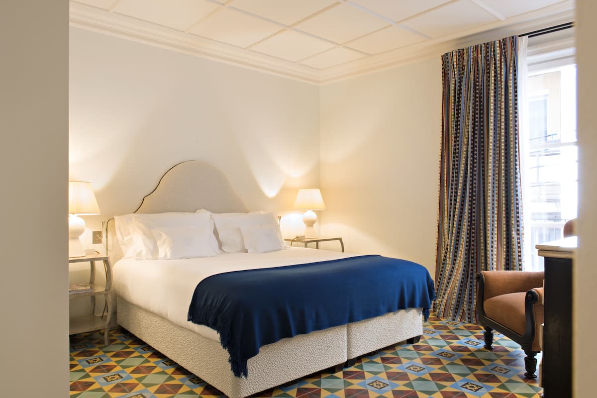A hotel room with a large bed, two bedside tables, a chair, and a patterned floor.