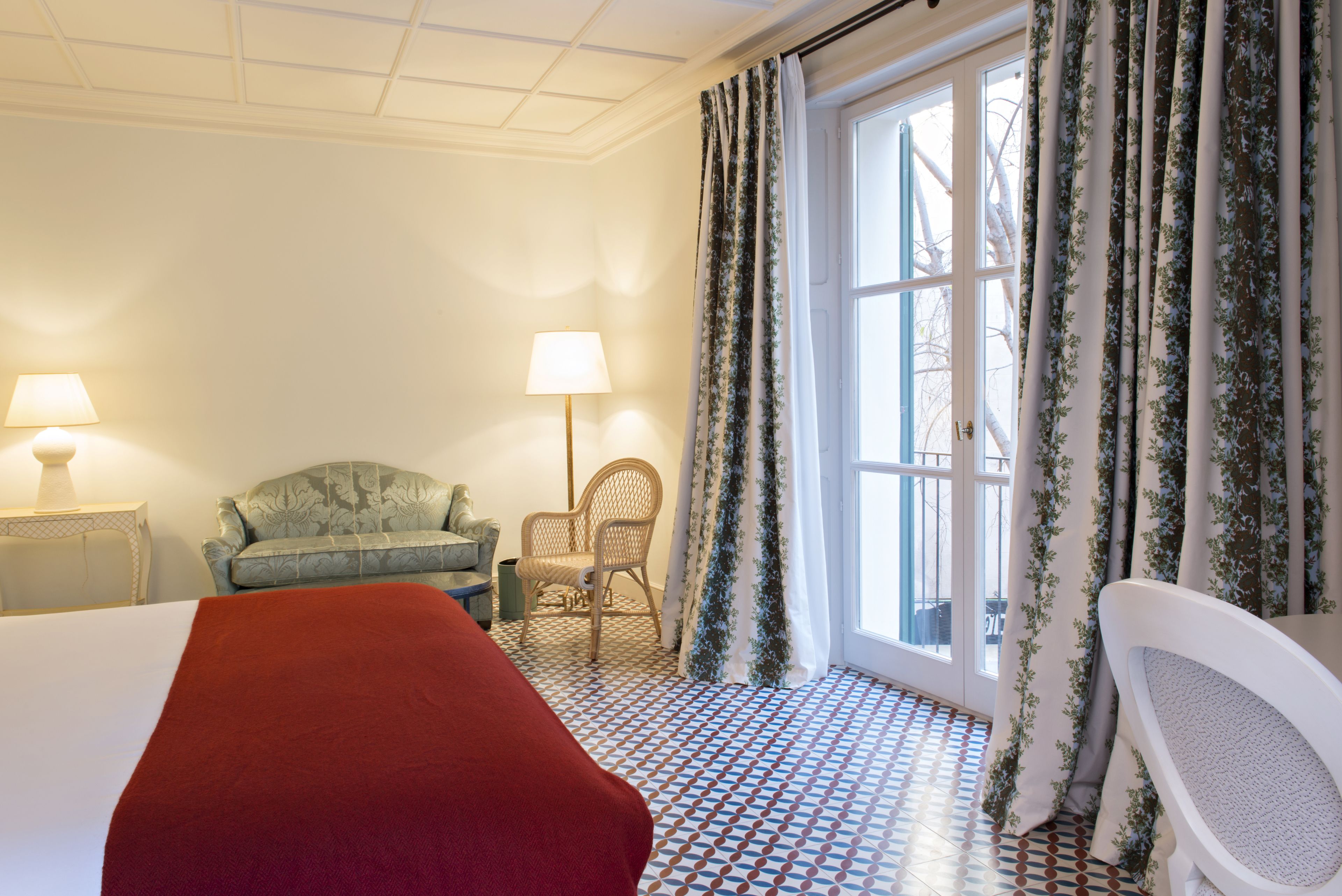 Une chambre d’hôtel avec un lit, deux chaises, une table et une fenêtre avec des rideaux.