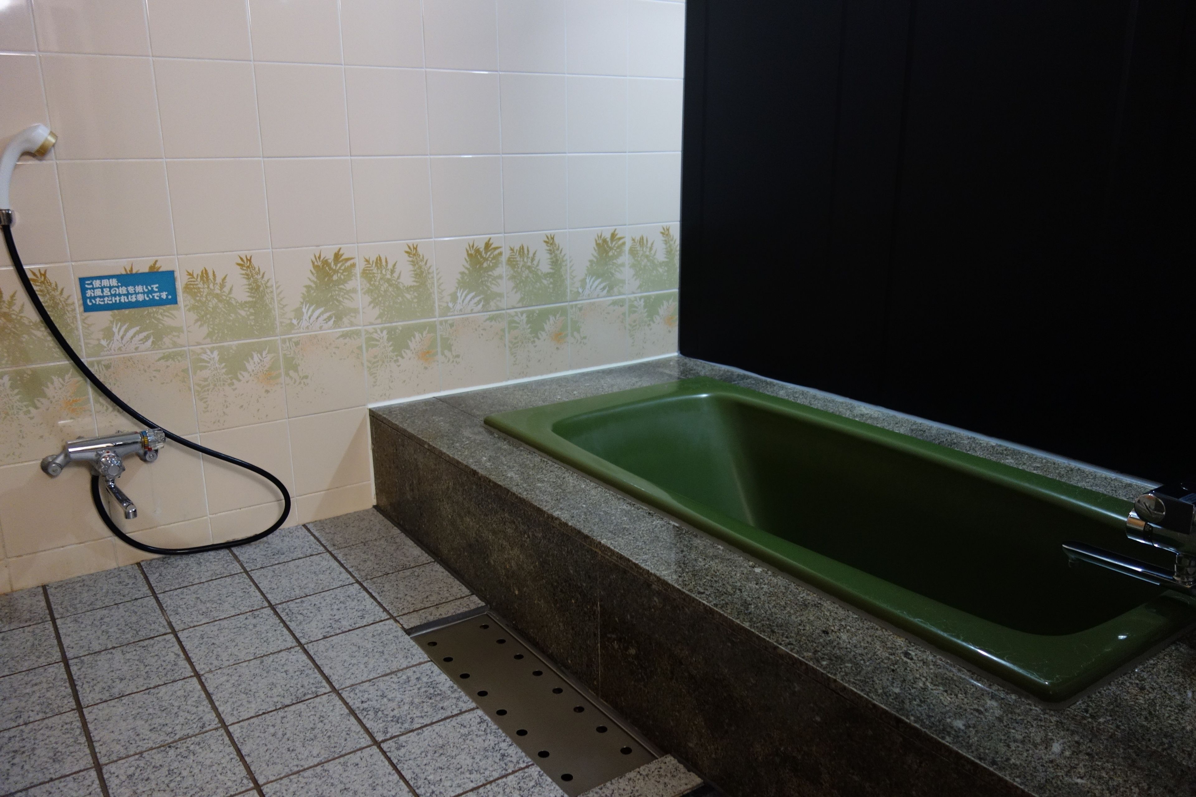 Un baño con un lavabo verde, ducha y piso de baldosas.