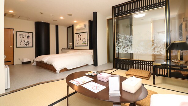 A hotel room with a bed, a round table with items, a large mirror, and artwork on the walls. - Sea Queen Kainan (Kainan)
