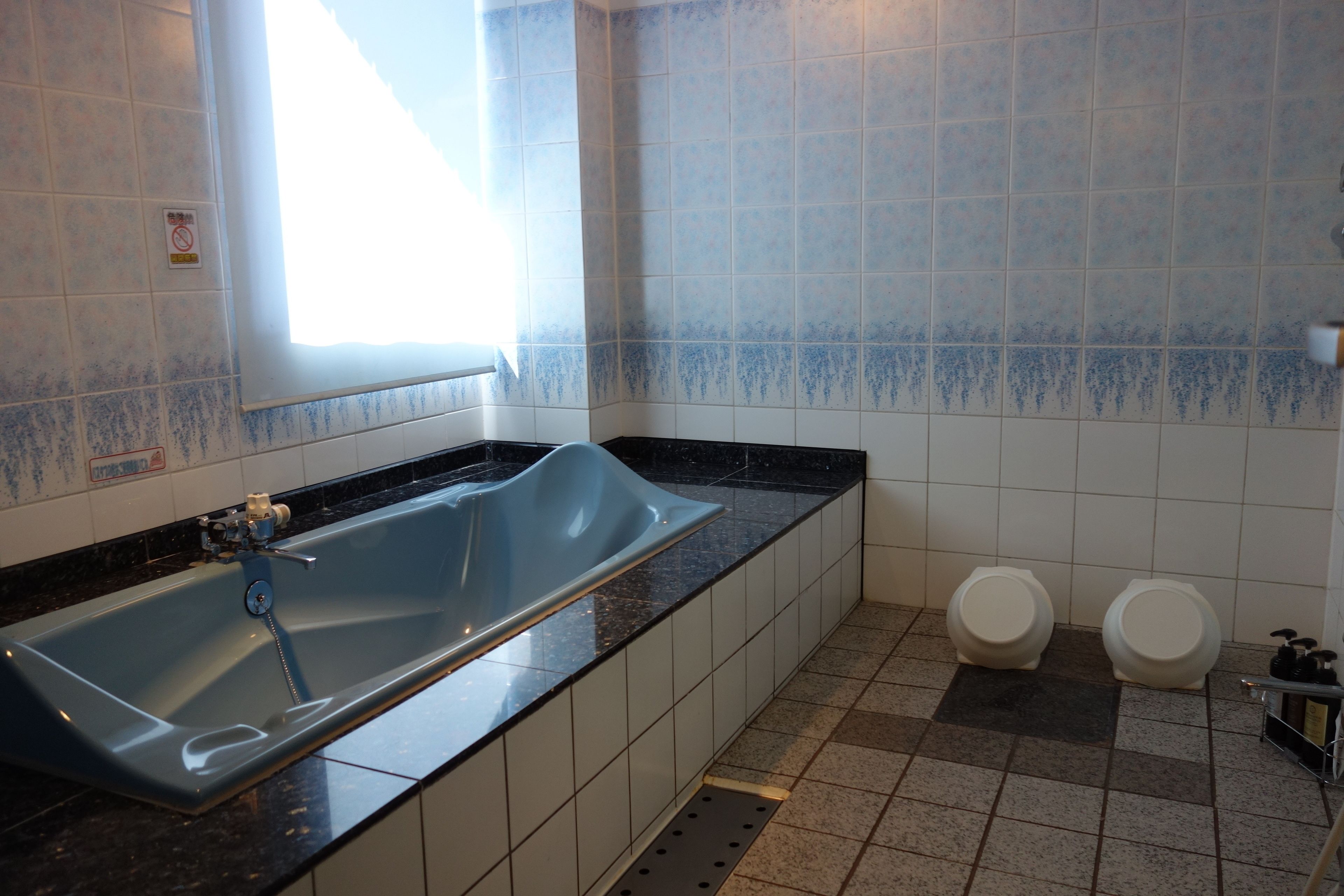 Une salle de bain avec une baignoire bleue, deux toilettes et une fenêtre.