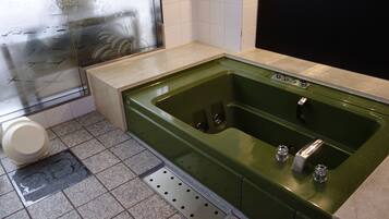 Un baño con una bañera verde, un inodoro y una zona de ducha.