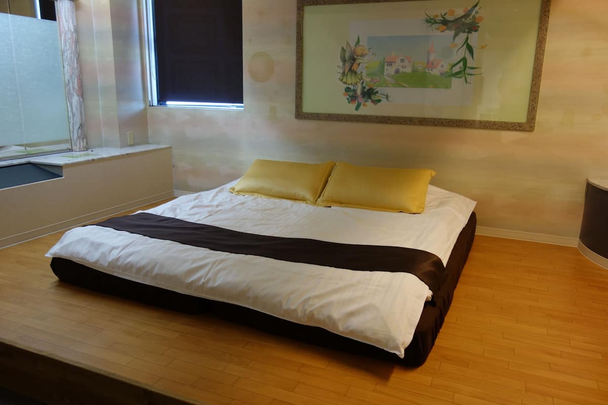 A neatly made bed with white and brown bedding, a yellow pillow, and a framed picture on the wall.