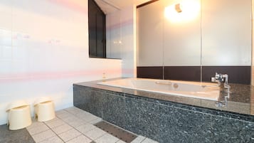 A modern bathroom with a large bathtub, a mirror, and two trash bins.