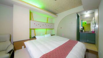 A hotel room with a bed, a chair, a vanity with a mirror, and a green-lit wall.
