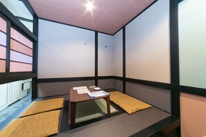 Una habitación de tatami con una mesa de madera baja, cojines y vistas a través de un celosía japonesa.