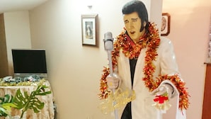 A room with a table covered in a beige cloth, a small plant, and a statue of a person with a microphone. - Hotel To (Wakayama)